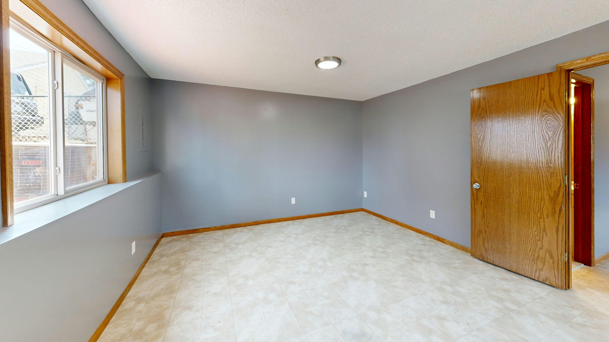 Spacious empty room with natural light from window and wooden door.